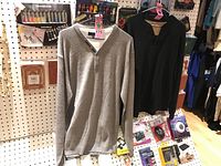 Two men's long sleeve Henley tops hanging on a pegboard wall with other items.