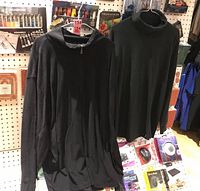 Two black men's tops displayed on hangers against a pegboard background: left is XXL half zip pullover, right is medium turtle neck.