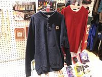 Two men's Henley style tops, navy blue Nantucket and red Haggar, hanging on display with electronics below.