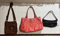 Three purses hanging on pegboard: brown Danier leather-like purse, coral Franco Sarto leather-like purse, black Polo Jeans Co. fabric purse