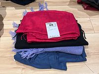 Stack of four folded items: red shawl, black scarf, lavender wool scarf, and dark blue scarf.