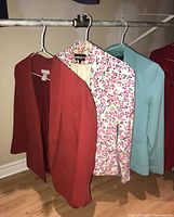 Three women's jackets hanging on a rod, visible are solid rust orange, floral print, and light blue jacket.