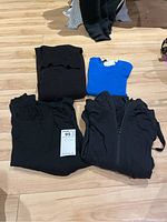 Four folded garments displayed on floor: black Forever 21 sweater dress, blue Zara short-sleeved sweater with tag, black MEC top, black Lululemon jacket with zipper