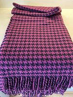 Full view of folded fuchsia and black houndstooth check lambswool blanket with twisted fringes at one end.