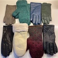 All eight pairs of mittens and gloves arranged on white surface showing different colors and materials including wool, leather and suede.