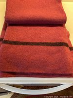 Folded view of the wine-colored wool blanket showing black stripe and dense texture.