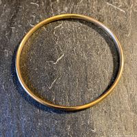Full view of the circular yellow gold bangle on dark background