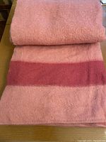 Folded wool blanket showing coral rose color and darker stripe detail.