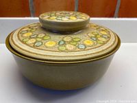 Front angle view of Franciscan lidded casserole dish showing dark mustard base and muted mustard lid with multi-colored circle pattern.
