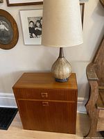 Front view of teak side table showing top surface, drawer front, and lower cabinet door with lamp placed on top.