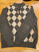 Full view of charcoal grey argyle sweater laid flat, front with diamond pattern and long sleeves