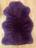 Top view of the full eggplant dyed sheepskin showing dense curly wool and irregular natural shape.