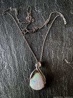 Full view of the sterling silver necklace with pear-shaped opal pendant on a dark surface.