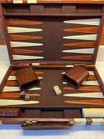 Backgammon board open showing felt playing surface with cinnamon and cream triangular points, dice cups, dice, and playing pieces arranged in trays.