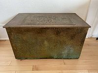 Front view of large rectangular copper-covered storage box with repousse lid detail, patina and hammered texture visible.