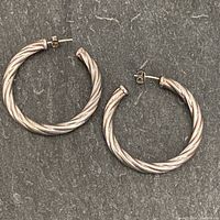Pair of silver twisted hoop earrings shown front view on dark background.