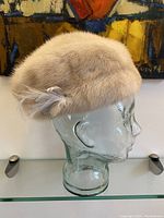 Side profile view of soft cream mink fur hat displayed on glass head, showing overall shape and texture.