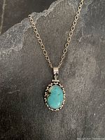 Full view of the sterling silver chain with oval turquoise stone pendant against a dark background.