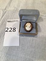 Front view of cameo ring in blue velvet jewelry box with lot number card