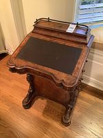 Front three-quarter view of desk showing hinged writing surface, carved supports and brass gallery rail