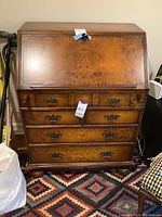 Front view of antique wooden writing desk with closed fold-down surface and four large drawers with metal handles.