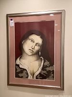 Framed lithograph portrait of a woman hung on a wall with silver frame and pink double matting.