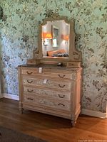 Front view of the antique dresser with four drawers and attached mirror on top against floral wallpapered wall.