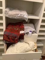 Three blankets including a red Cecch Cecch wool blanket with fringe, a light colored Calvin Klein blanket, and an LL Bean comforter in a drawer.