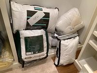 Six pillows and bedding items arranged in a closet shelf with packaging labels visible showing brands and types