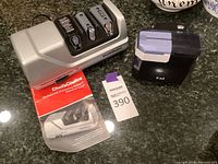 Photo of Chef's Choice sharpening station with three sharpening slots, manual, and Kai electric sharpener side by side on a counter.