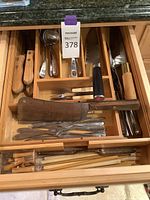 Drawer with various wooden and metal utensils arranged, including knives, forks, and cutting utensils