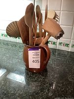 Wooden kitchen utensils stored upright in a brown ceramic jug on a kitchen counter.