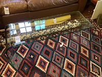 Curved glass coffee table with smooth edges resting on a patterned rug, showing its length and transparency.