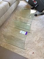 Two modern clear glass end tables placed on carpet, showing curved U-shape design and smooth polished edges.