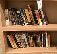 Two wooden shelves filled with various books in good used condition, showcasing titles across different genres including literature, cooking, and memoir.
