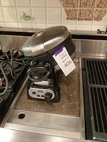 Side view of the KitchenAid waffle maker with wrapping cord and stainless steel lid.