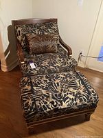 Front three-quarter view of chair with leopard print upholstery, matching ottoman, and small zebra pattern throw pillow