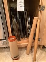 Photo showing vertical stack of metal baking sheets and trays plus a silicone baking mat on the floor.