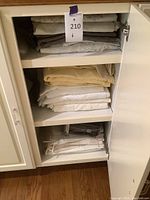 Photo showing neatly folded grey and light patterned bed linens on a shelf inside a cabinet