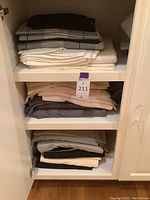 Folded bed linens stacked on shelves inside a white cabinet, showing multiple colors and patterns including solids and checks.