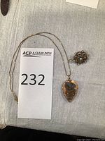 Overview of necklace with leaf-shaped butterfly locket on chain and circular stone and pearl brooch