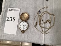 Pocket watch open showing white enamel dial, inner case and chain items