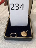 Ring and locket displayed inside an open jewelry box with dark blue velvet interior.
