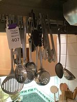 Photo of hanging stainless steel kitchen utensils including slotted spoons, ladle, and tongs.
