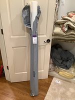 Full view of a tall roll of wallpaper in torn gray plastic wrapping leaning against a closed white door, with part of a closet visible beside it.