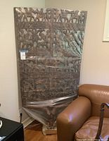 Full view of the carved wooden panel sculpture leaning against wall.