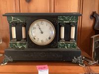 Full frontal view of antique mantel clock showing wood case with marble accents, roman columns and metal claw feet.