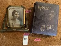 Overall view of antique Holy Bible with detached front cover and a vintage photo in decorative frame side by side on carpeted surface.