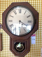Full frontal image of the Ansonia octagonal wall clock showing wooden frame, dial with Roman numerals, glass covering, and lower pendulum case with brass pendulum inside.