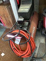 Orange Craftsman air compressor with coiled air hoses on top, showing full unit.